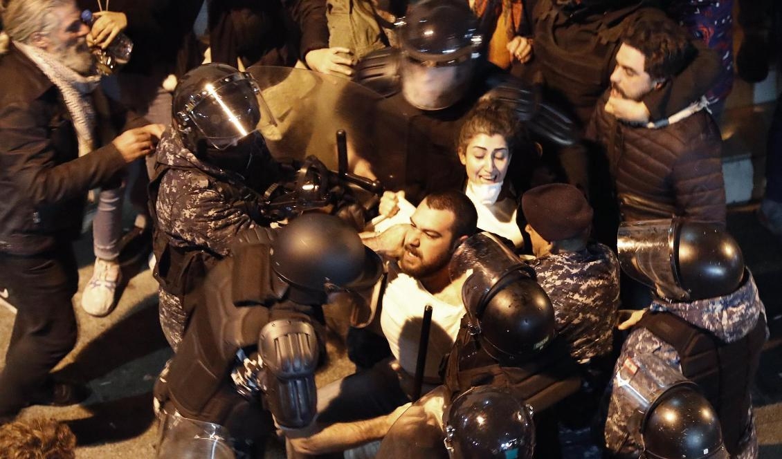 
Kravallpolis griper demonstranter som protesterar utanför en polisstation i Beirut. Foto: Hussein Malla/AP/TT                                                