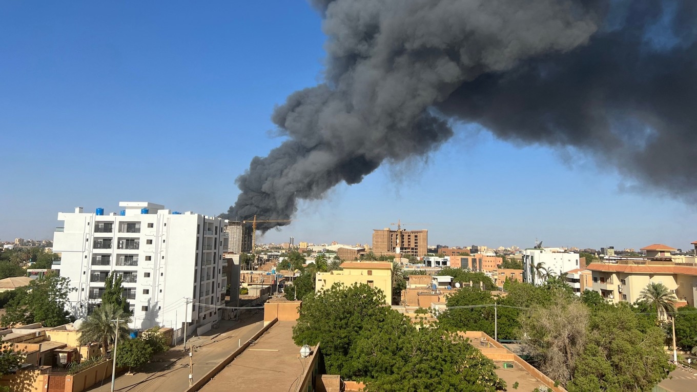 En rökpelare stiger upp bakom byggnader nära flygplatsområdet i Sudans huvudstad Khartoum den 19 april 2023 i samband med strider mellan armén och paramilitären. Foto: AFP via Getty Images