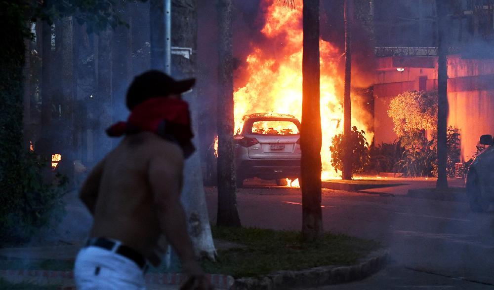 Ett fordon brinner och en demonstrant kastar sten mot polisen under upplopp i protest mot gripandet av guvernör Camacho i Santa Cruz i Bolivia den 30 december. Foto: Rodrigo Urzagasti/AFP via Getty Images