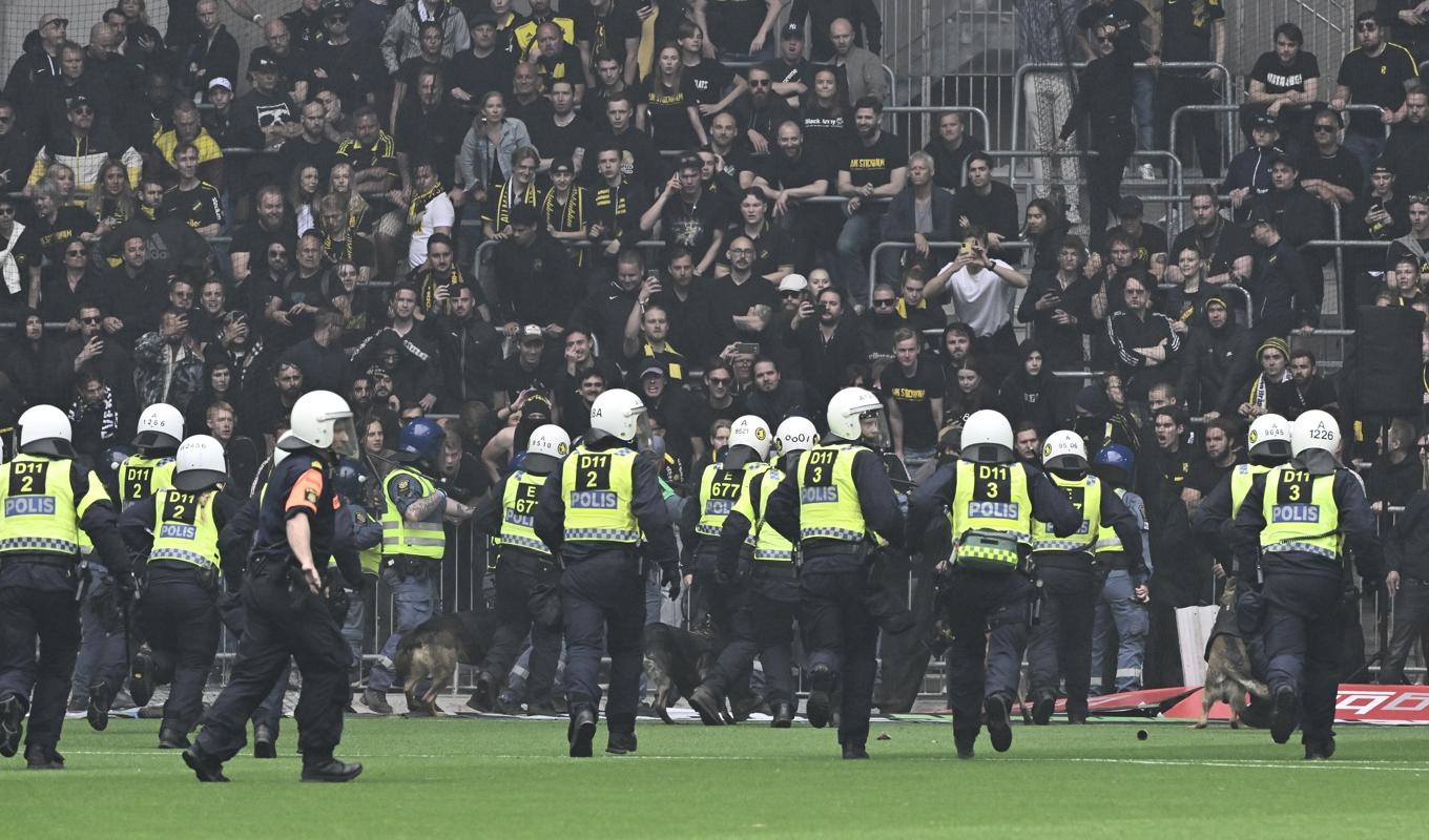 Kravallpolis i full skyddsutrustning och med hundar motar tillbaka maskerade AIK-supporters som försöker storma planen i vårens derby på Tele2 Arena. Foto: Jonas Ekströmer/TT