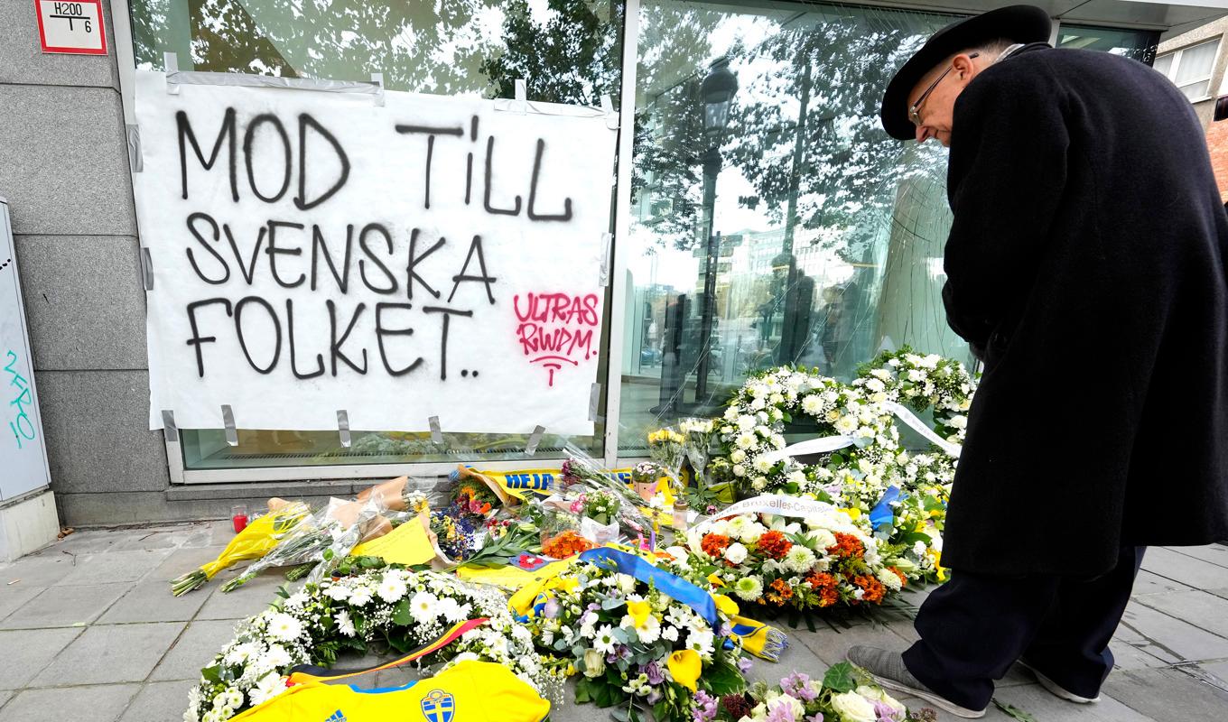 En man studerar blommor, kransar och fotbollskläder som lagts ned vid brottsplatsen i Bryssel där två svensk supportrar sköts till döds i måndags. Foto: Martin Meissner/AP/TT