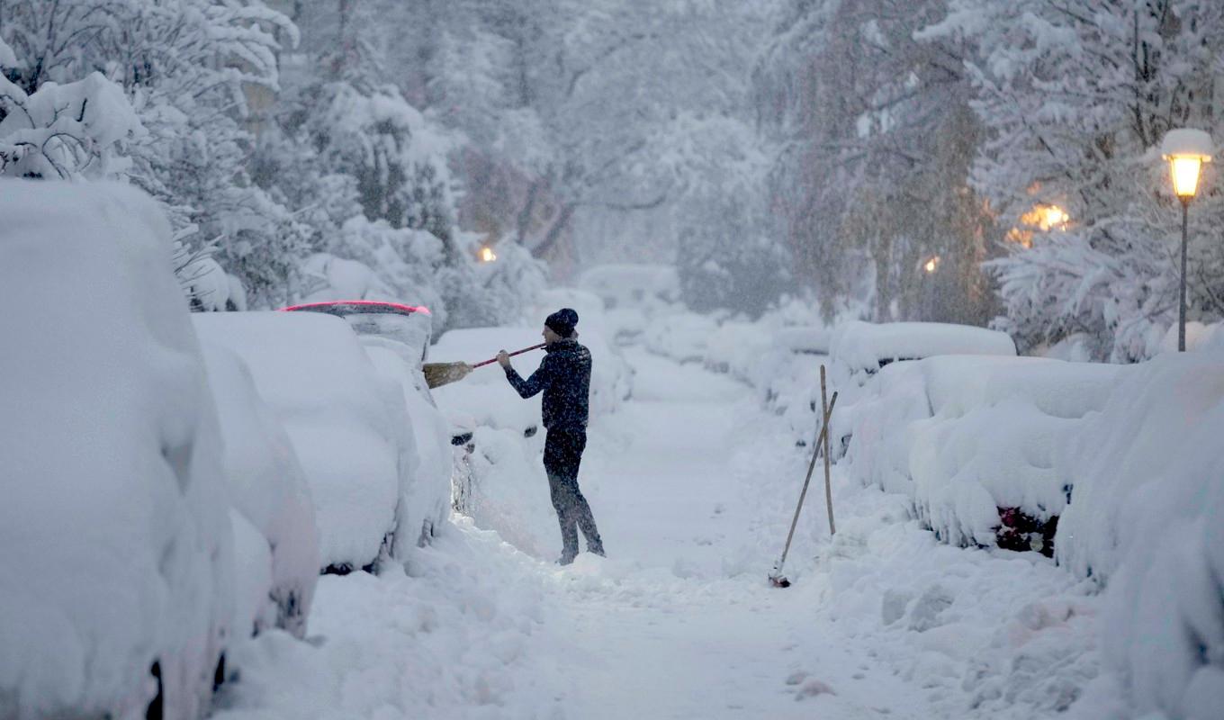 En man i München tar bort snö från sin bil efter de kraftiga snöfall som bland annat dragit in över i södra Tyskland. Foto: Matthias Schrader/AP/TT