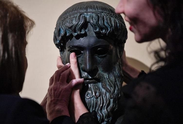 En synskadad kvinna känner på en kopia av en antik grekisk staty. Antiken kan kännas både nära och långt borta på samma gång. Foto: Louisa Gouliamaki/AFP via Getty Images