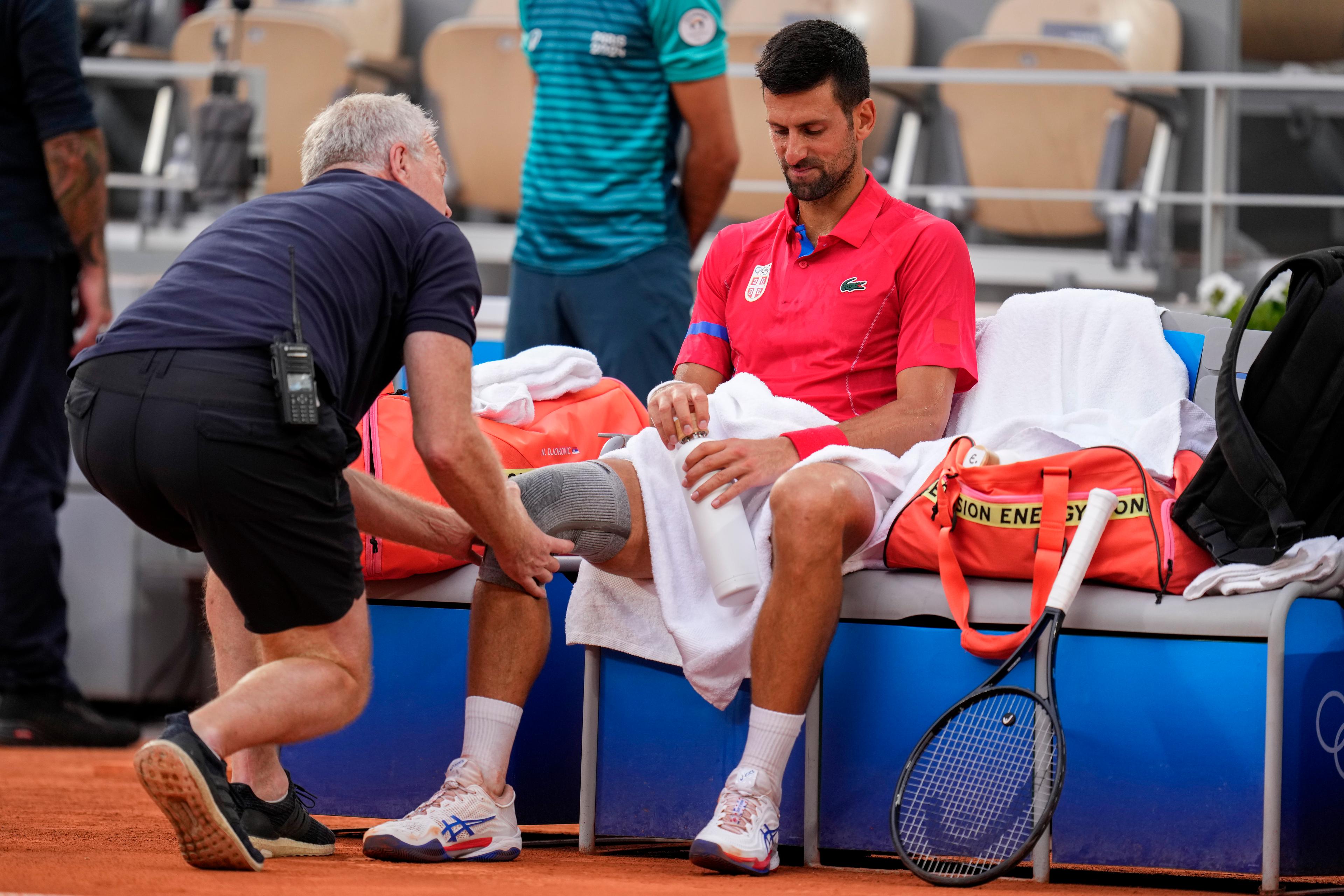 Novak Djokovic får läkarvård för en knäskada under matchen mot Stefanos Tsitsipas på torsdagen. Foto: Manu Fernandez/AP/TT