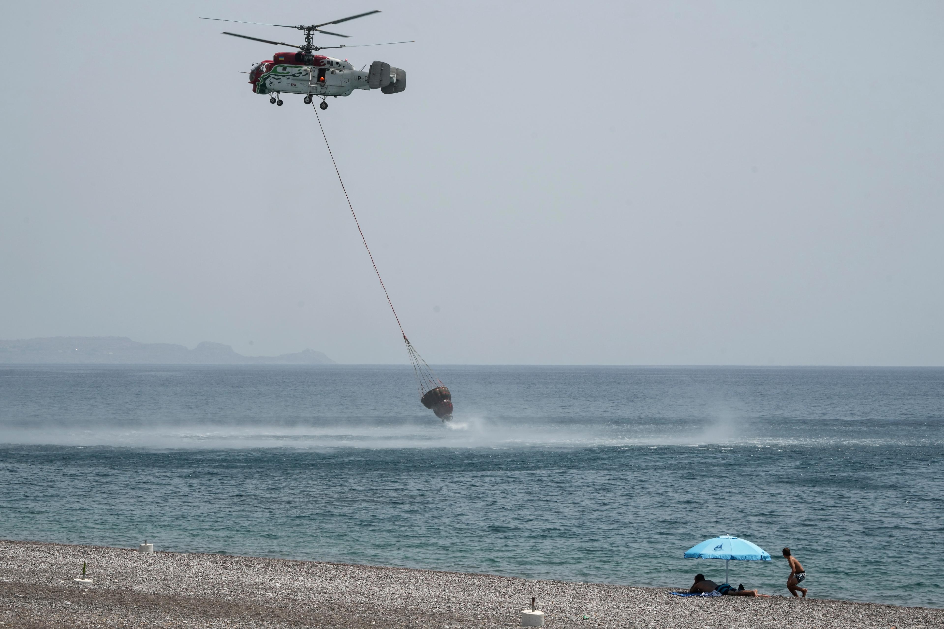 En helikopter som samlar upp vatten för att bekämpa en skogsbrand på Rhodos den 27 juli. Foto: Petros Giannakouris/AP/TT