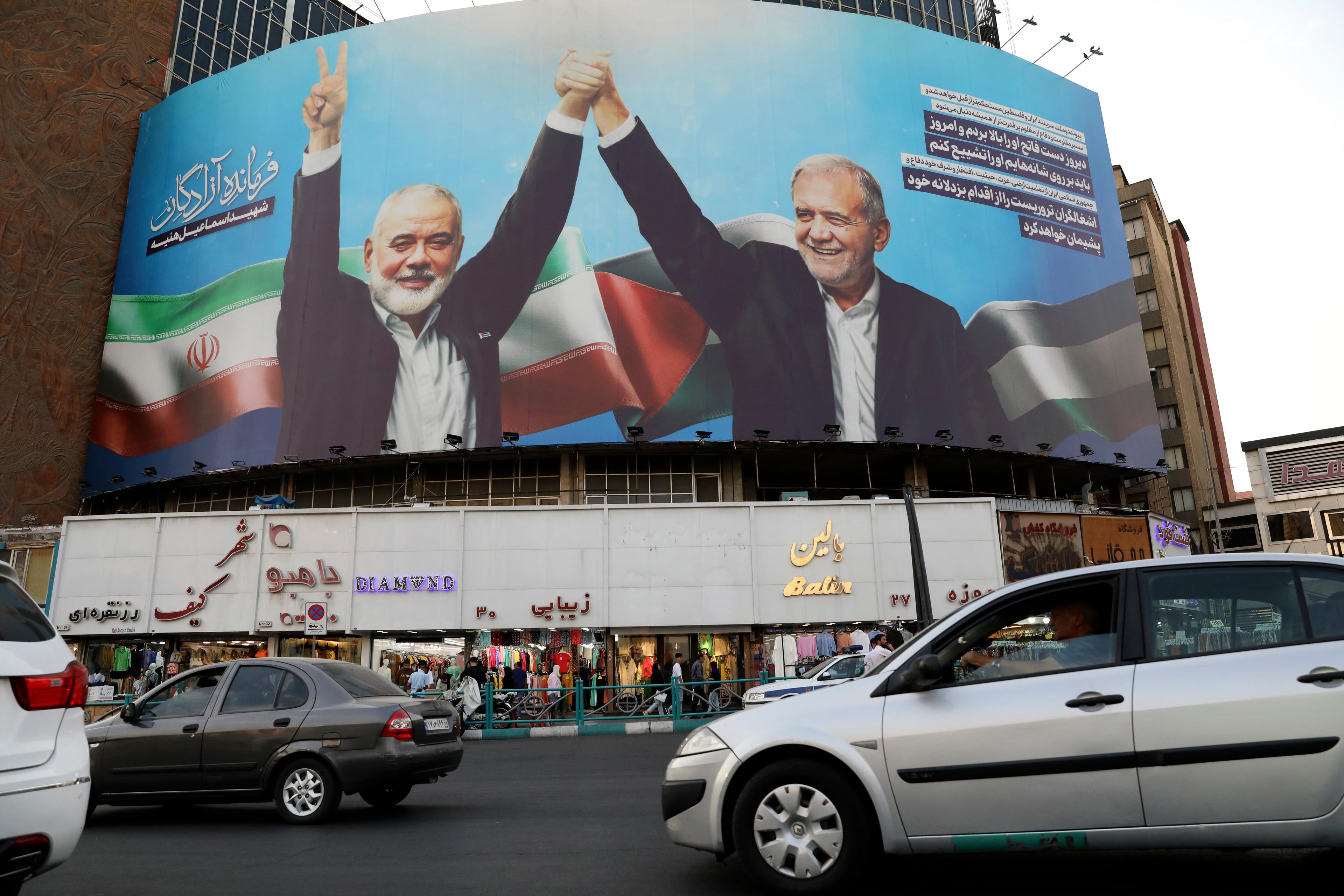 En stor bild i Teheran föreställande den döde Hamasledaren Ismail Haniya och Irans nye president Masoud Pezeshkian den 5 augusti. Foto: Vahid Salemi/AP/TT