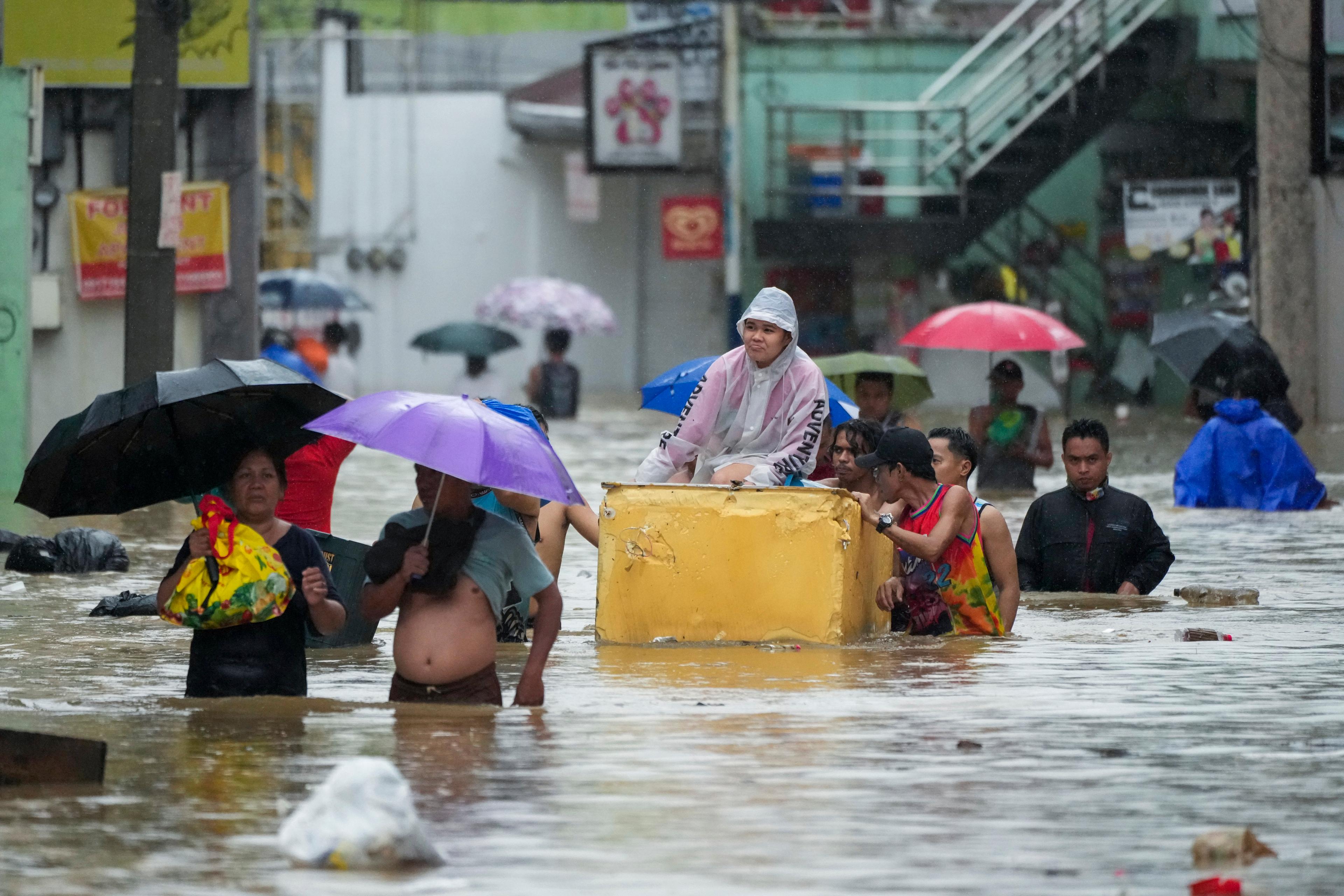 En person åker på ett gammalt kylskåp medan andra vadar genom den översvämmade gatan i kommunen Cainta i Filippinerna. Bild från måndagen. Foto: Aaron Favila/AP/TT