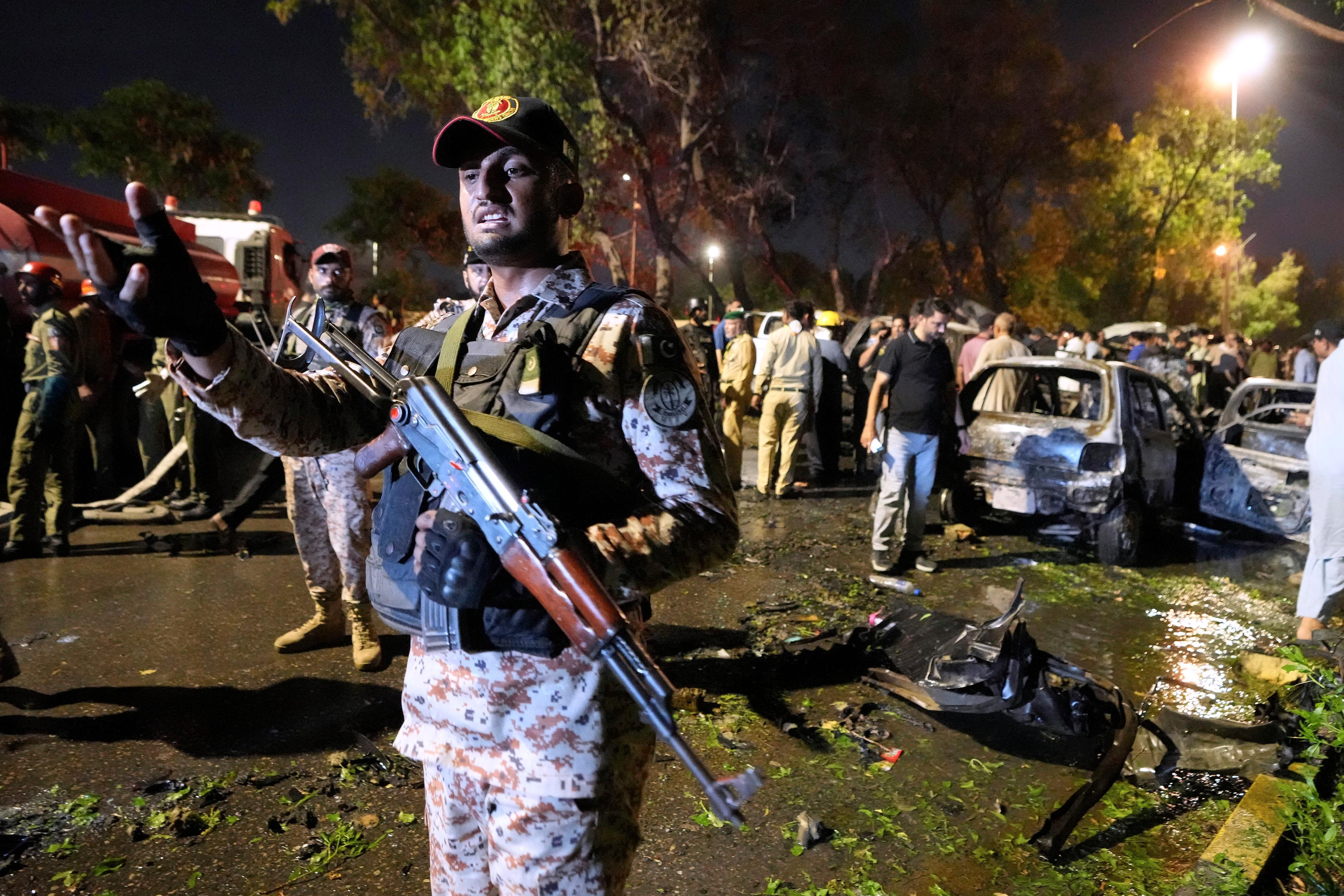 En paramilitär soldat gestikulerar mot medier vid platsen där explosionen utanför Karachis flygplats inträffade. Foto: Fareed Khan/AP/TT