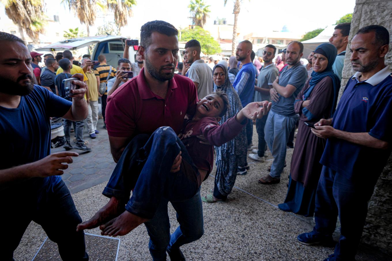 En man bär ett barn som skadats i en israelisk attack mot en skolbyggnad i Dayr al-Balah i Gazaremsan på torsdagen. Foto: Abdel Kareem Hana/AP/TT