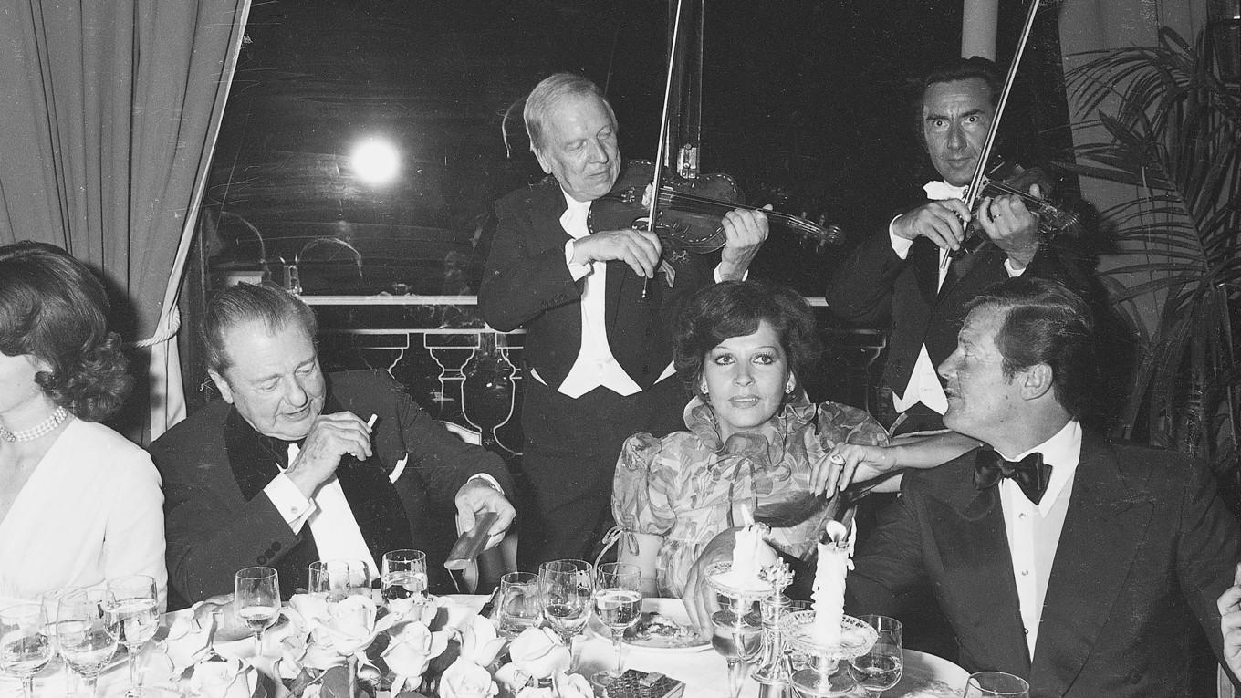 Roger Moore med sällskap äter middag på restaurang Le Grill på Hôtel de Paris i Monte Carlo, 1977. Bredvid Moore sitter den franska sångerskan Françoise Hardy som gick bort den 11 juni 2023. Hardy (1944–2023) representerade just Monaco i Eurovision Song Contest 1963 med låten "L’amour s’en va" och kom på en delad femte plats. I Sverige låg låten etta på branschtidningen Show Business försäljningslista. 1969 fick hon ytterligare en svensk framgång då hennes låt ”Comment te dire adieu” gick in på Tio i topp-listan. Foto: Archives Monte-Carlo-SBM