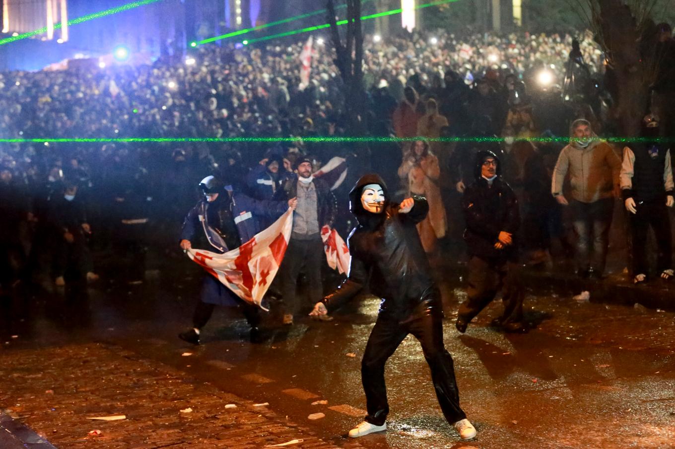 En maskerad demonstrant kastar något mot polisen under protesterna utanför parlamentet i Tbilisi. Foto: Zurab Tsertsvadze/AP/TT