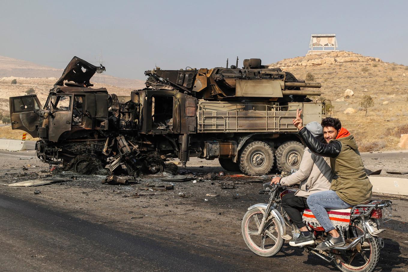 En syrier ger segertecknet framför ett utbränt militärfordon, förstörd i anslutning till ett israeliskt angrepp mot Damaskus. Foto: Omar Sanadiki/AP/TT