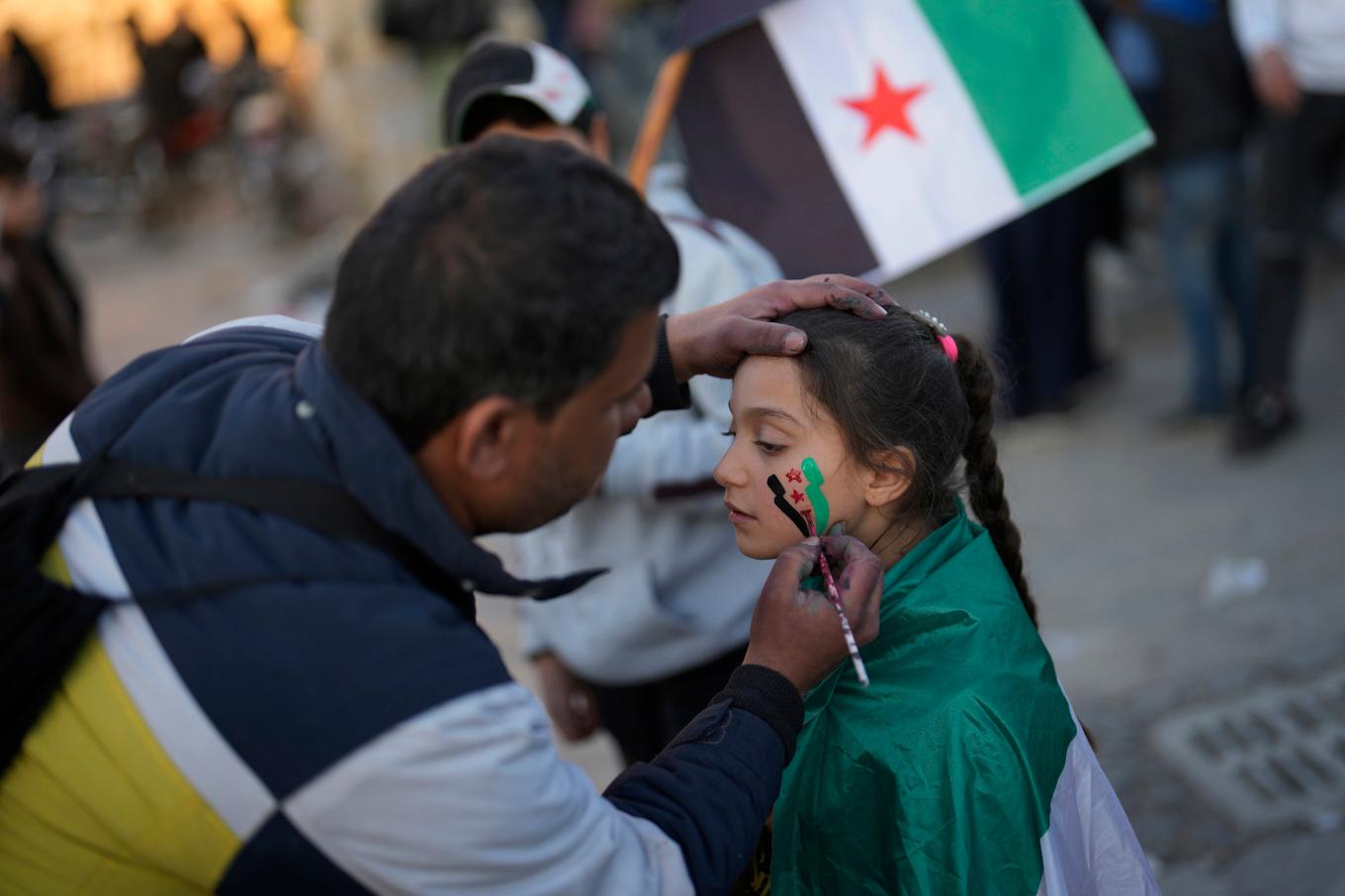 En man målar den syriska oppositionens flagga på en flickas kind i Aleppo i lördags. Foto: Khalil Hamra/AP/TT