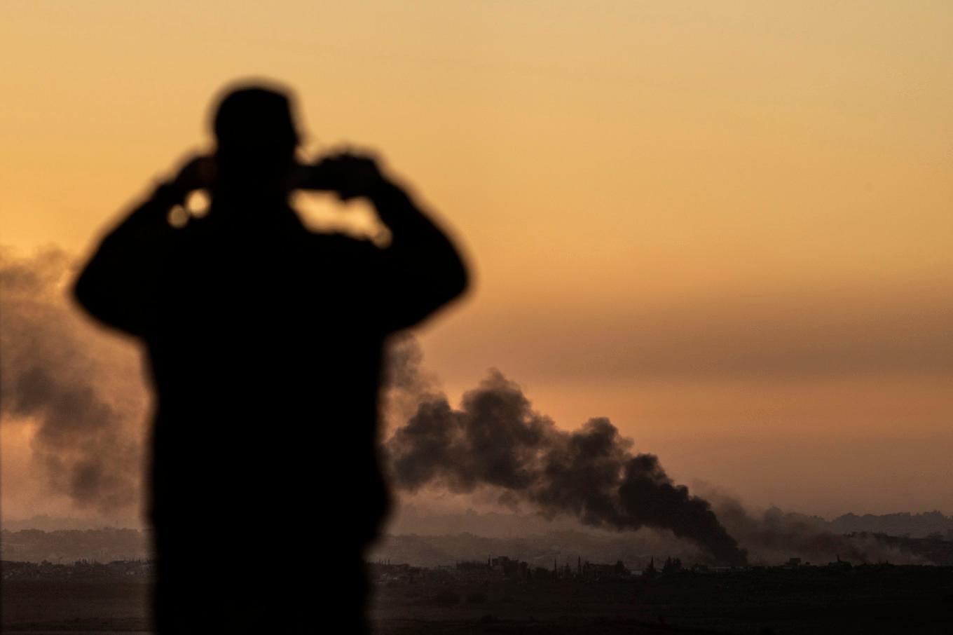 Rök stiger från en explosion i Gazaremsan i måndags. En man i Sderot i Israel följer det på avstånd. Foto: Ariel Schalit/AP/TT