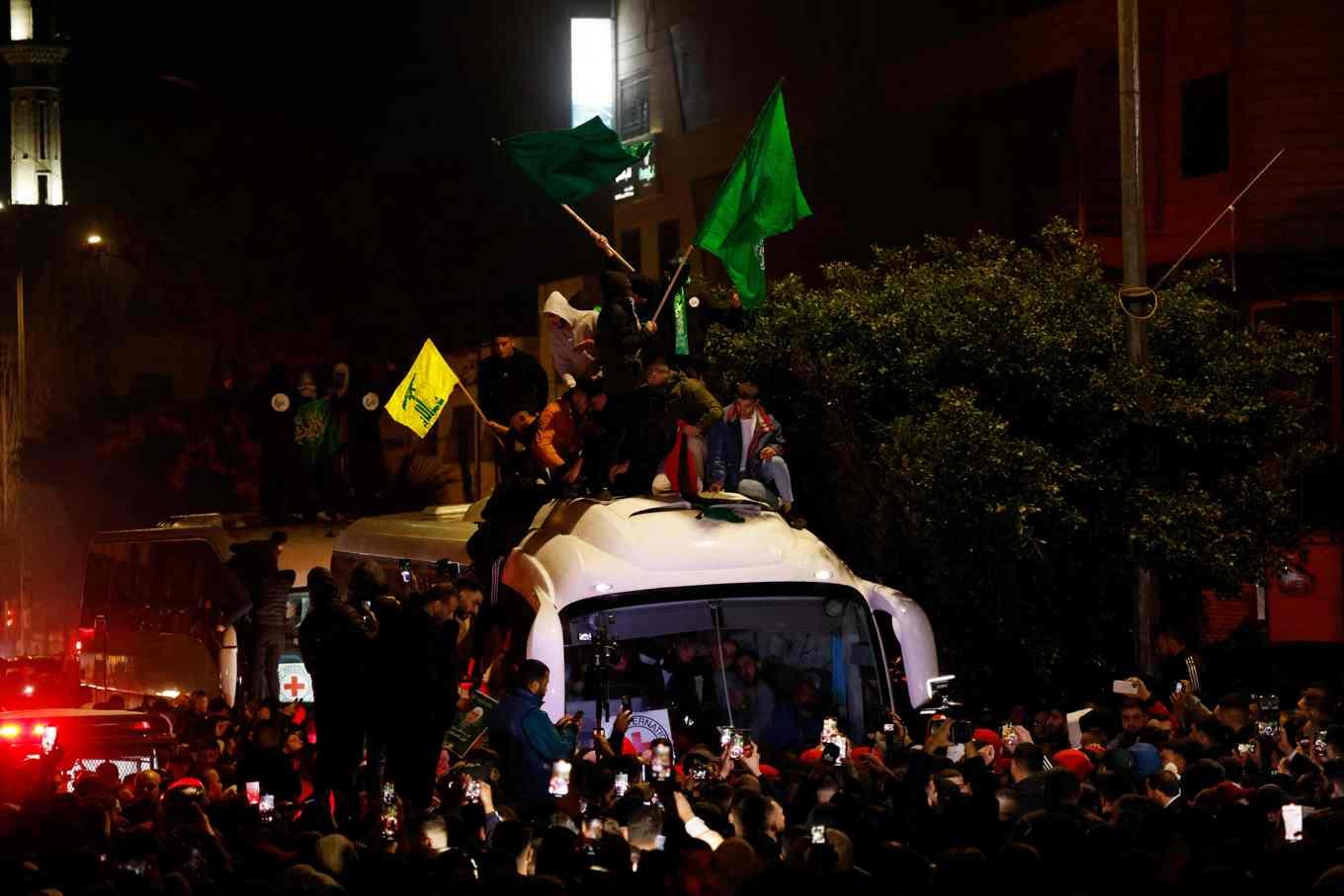 Röda korsets buss med frisläppta palestinier i Beitunia utanför Ramallah på Västbanken. Män som viftar med Hamas gröna flagga och Hizbollahs gula har klättrat upp på bussen. Foto: John Wessels/AFP/TT