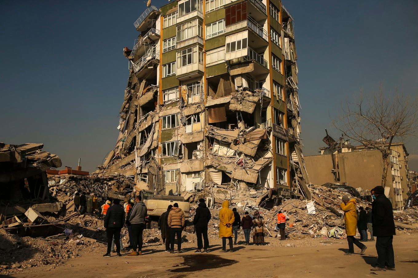 Människor står vid en kollapsad byggnad i den turkiska staden Kahramanmaras dagar efter jordbävningen den 6 februari 2023. Foto: Emrah Gurel/AP/TT