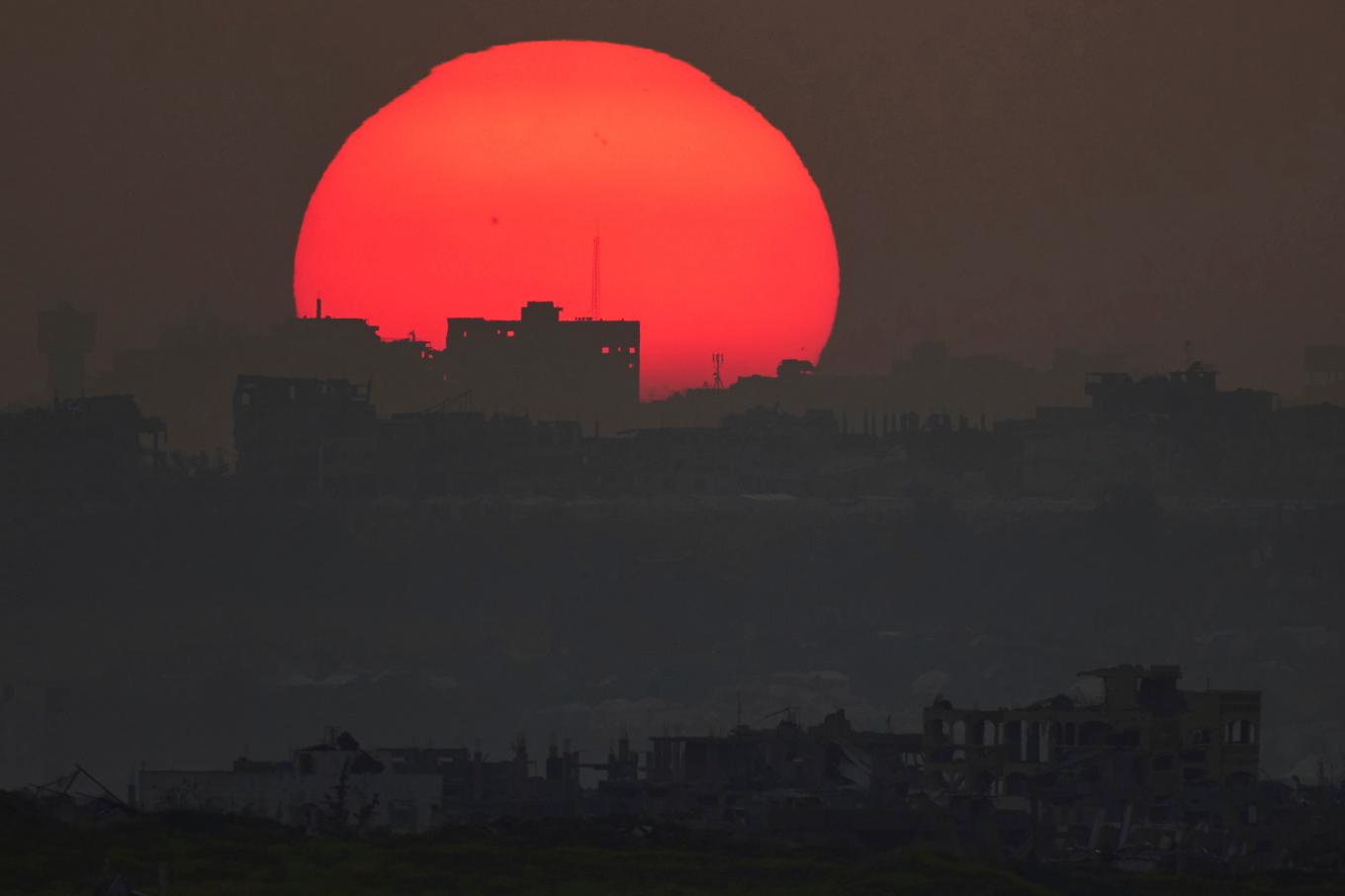 Solen går ned bortom förstörda huskroppar i krigshärjade Gazaremsan. Bilden togs från israelisk mark på måndagskvällen. Foto: Leo Correa/AP/TT