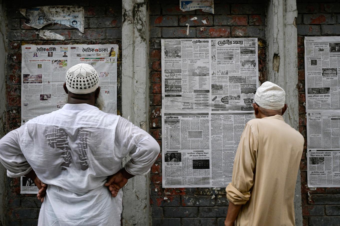 Män läser tidningar som satts upp på en vägg i Bangladesh huvudstad Dhaka. Bilden är tagen i augusti, då premiärminister Sheikh Hasina tvingades bort från makten. Foto: Fatima Tuj Johora/AP/TT