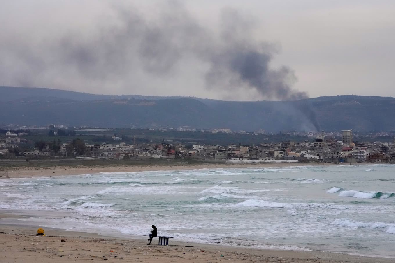 En man syns på stranden medan rök stiger efter en israelisk attack i en by i södra Libanon i lördags. Foto: Hussein Malla/AP/TT
