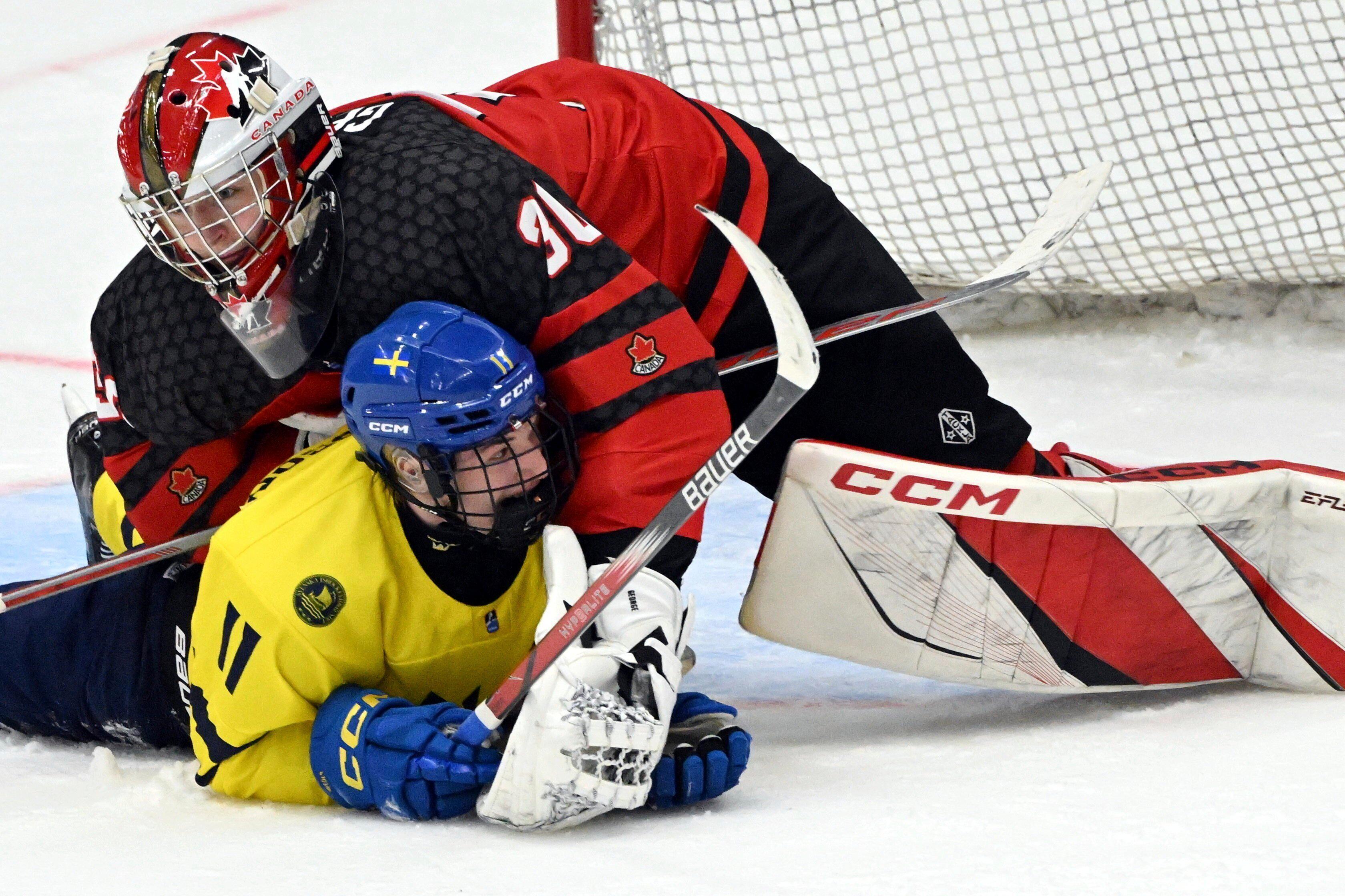 Sverige på fall. Lucas Pettersson hamnar under Kanadas målvakt Carter George i semifinalen i U18-VM. Foto: Jussi Nukari/AP/TT