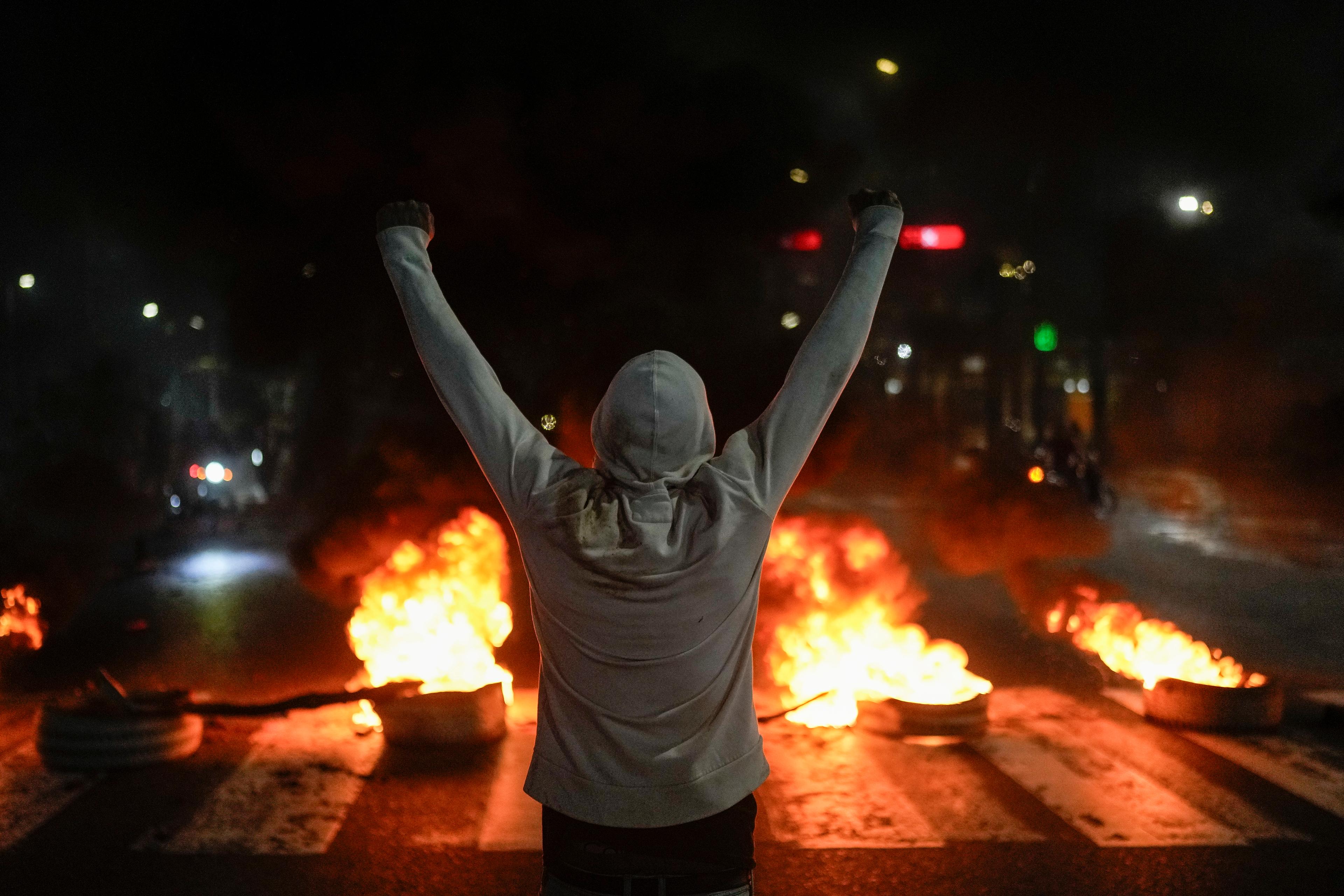 En demonstrant framför brinnande bildäck i Venezuelas huvudstad Caracas på måndagen. Foto: Matias Delacroix/AP/TT