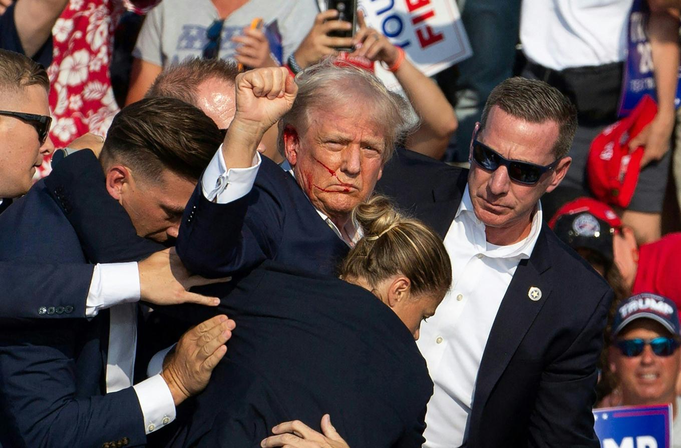 Den republikanske presidentkandidaten Donald Trump ses med blod i ansiktet omgiven av säkerhetspersonal när han tas av scenen vid ett kampanjevenemang på Butler Farm Show Inc. i Butler, Pennsylvania, den 13 juli 2024. Donald Trump träffades i örat i ett uppenbart mordförsök av en beväpnad man vid ett kampanjmöte i lördags. Den som sköt och en åskådare dödades, och två åskådare skadades allvarligt. Bild: REBECCA DROKE/AFP via Getty Images.