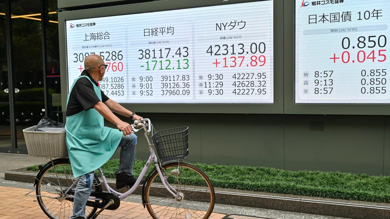 En man på cykel stannar till för att titta på en elektronisk aktietavla längs en gata i Tokyo den 30 september. Foto: Richard A. Brooks/AFP via Getty Images