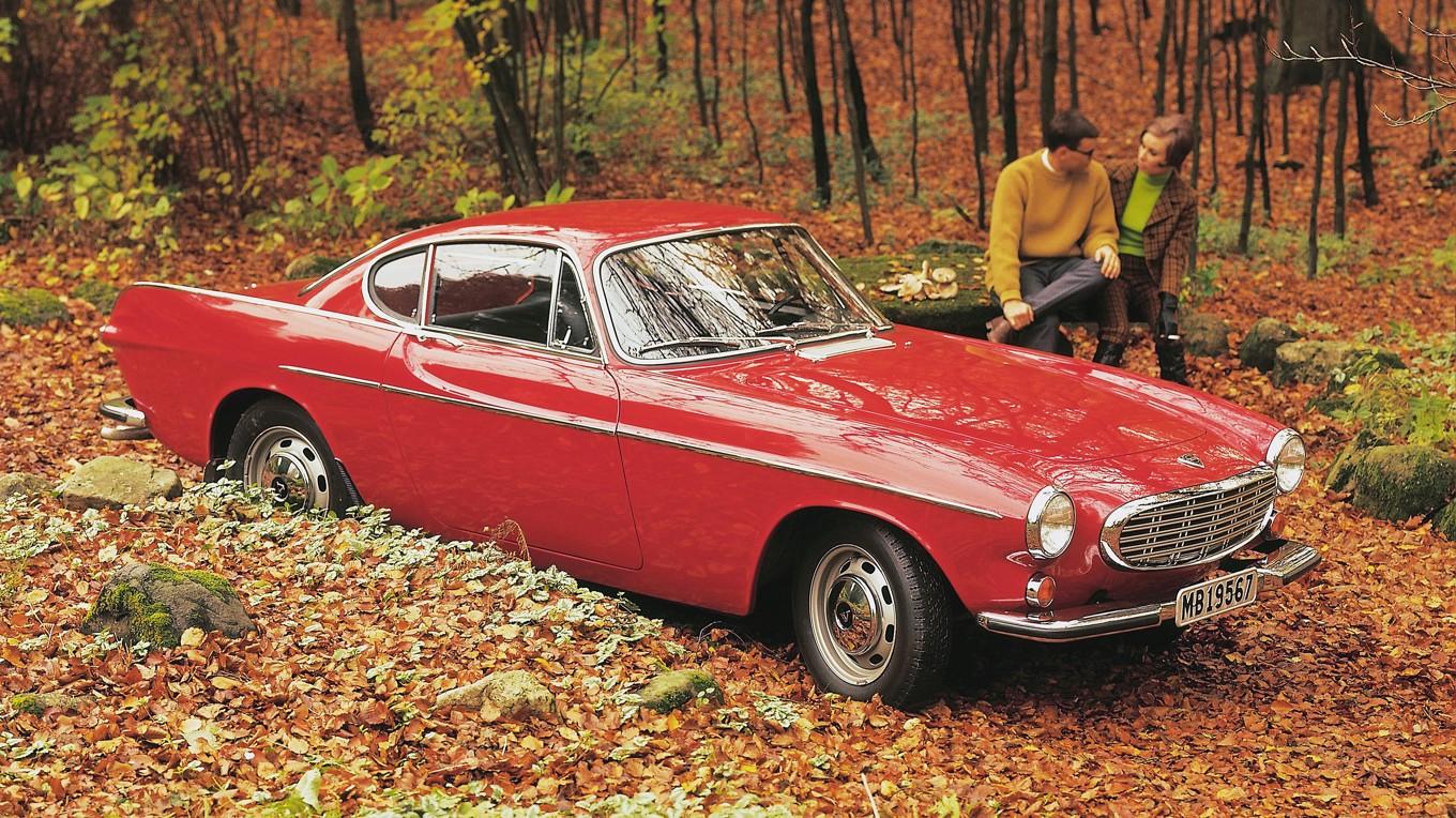 Med sin tidlösa design och imponerande tekniska specifikationer har P1800 blivit en älskad klassiker som fortsätter att närmast trollbinda bilentusiaster världen över. Volvo P1800 är känd för sin slanka och sportiga siluett. Den har en lång front med en kort bakdel, vilket ger bilen ett aggressivt men ändå elegant utseende. De rundade formerna och den låga taklinjen bidrar till bilens aerodynamik och stil. Frontgrillen har en distinkt Volvo-logotyp och de stora strålkastarna ger bilen en uttrycksfull look. Färgalternativen varierade under åren, men klassiska färger som röd, vit och grön är de mest eftertraktade bland samlare i dag. Lacken var av hög kvalitet, vilket hjälpte bilen att behålla sitt utseende genom åren. Volvo P1800 kom initialt med en 1,8-liters fyrcylindrig motor, vilket gav en effekt på omkring 100 hästkrafter. Detta var en bra prestanda för sin tid och gav bilen en toppfart på cirka 185 km/h. Med en manuell växellåda var acceleration från 0 till 100 km/h möjlig på omkring 10 sekunder. Under åren uppgraderades motorn till en 2,0-liters variant med insprutning i P1800E-modellen, vilket ökade effekten till omkring 130 hästkrafter. Denna uppgradering förbättrade inte bara prestandan, utan också bränsleekonomin. P1800:S Chassi är robust och välbyggt, vilket ger en stabil körupplevelse. Bilen har en dubbel A-upphängning fram och en bladfjäder bak, vilket ger en fin balans mellan komfort och sportig känsla. Den låga tyngdpunkten bidrar också till bättre köregenskaper, särskilt i kurvor. Bromssystemet var också avancerat för sin tid, med skivbromsar fram och trumbromsar bak, vilket gav bilen bra bromsprestanda. P1800 var inte bara en estetiskt tilltalande bil, utan även en teknologisk framgång. Volvo var en av de första tillverkarna att introducera säkerhetsfunktioner som trepunktsbälten och en styv kaross-struktur för att skydda passagerarna vid kollisioner. Dessa funktioner var banbrytande för sin tid och har sedan dess blivit standard inom bilindustrin.
Foto: Volvo Car Group