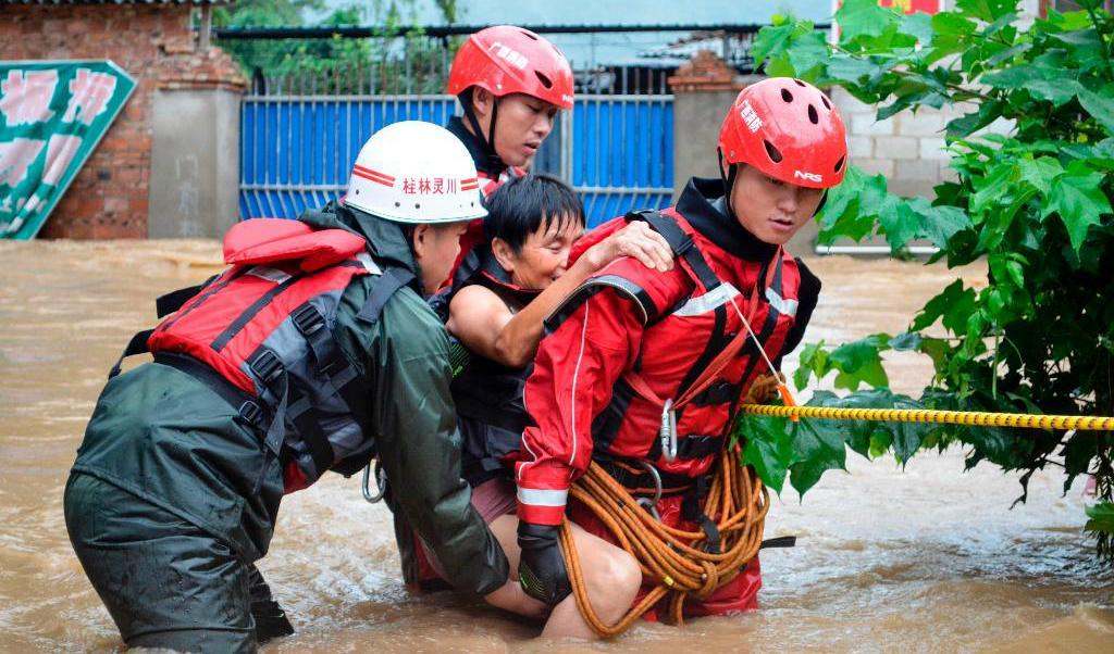 
Räddningsarbetare hjälper en äldre kvinna ta sig över en översvämmad väg i Guilin, Guangxi. Foto: STR/AFP/TT                                            