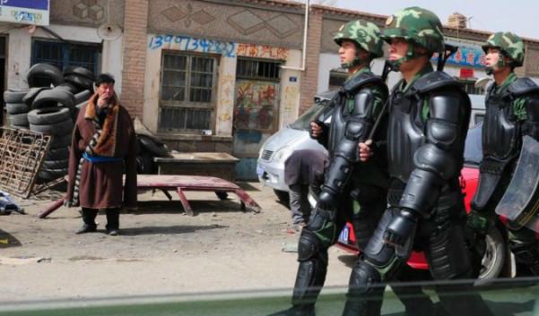 Skyltar på kinesiska syns på denna bild av en tibetansk man i traditionella kläder som betraktar kinesiska paramilitärer i kravallutrustning i Guomaying på den tibetanska platån. Foto: Frederic J. Brown/AFP/Getty Images