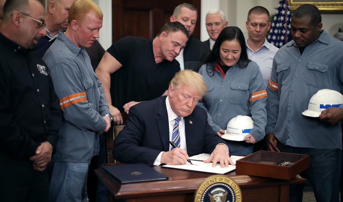 




USA:s president Donald Trump skriver under beslutet om de nya tullavgifterna på stål och aluminium i Vita huset, omgiven av stål- och aluminiumarbetare, 8 mars 2018. Foto: Chip Somodevilla/Getty Images                                                                                                                                                                                                                            