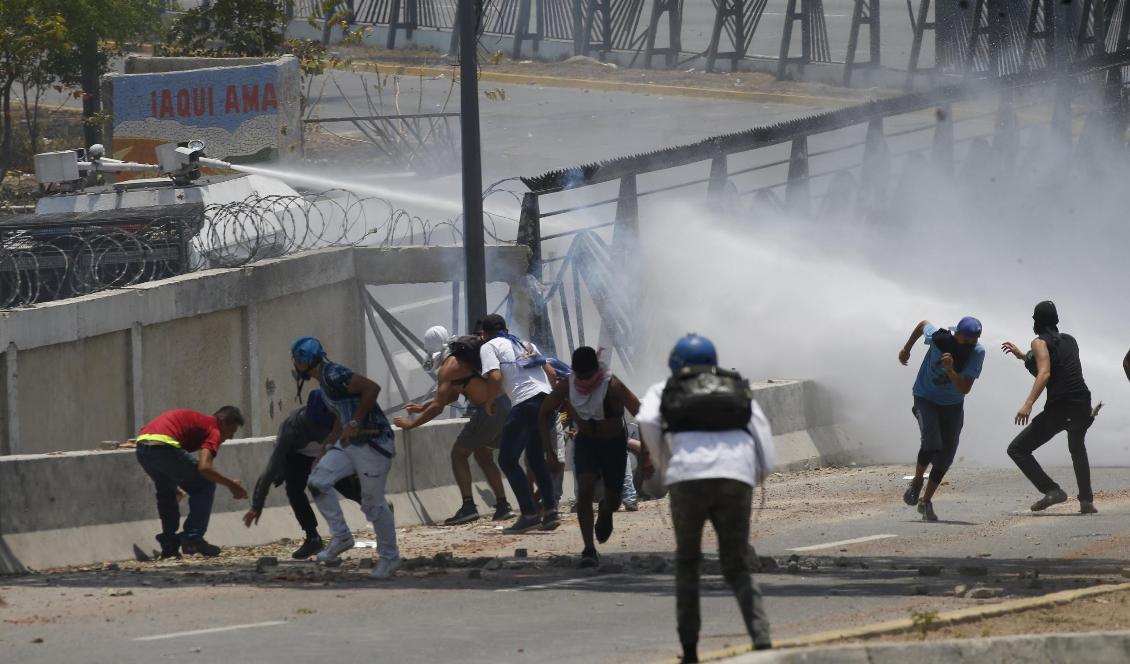 Demonstranter möts av vattenkanoner vid flygbasen La Carlota. Foto: Ariana Cubillos/AP/TT