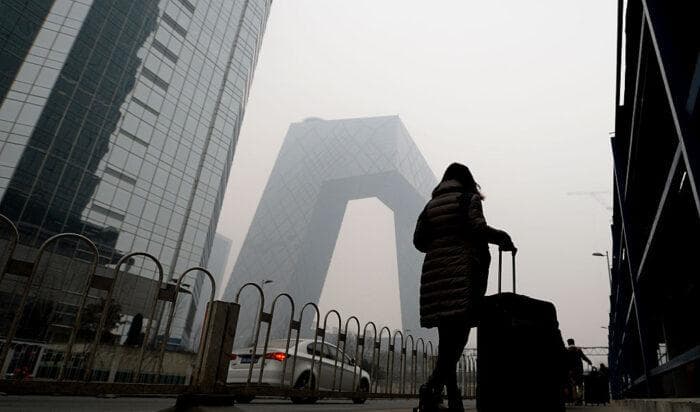 En kvinna passerar det nya CCTV-tornet inhöljt i tät smog i Peking den 8 dec. 2015. Foto: STR/AFP via Getty Images.