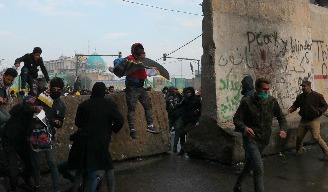 
Regeringskritiska demonstranter tar skydd bakom betongavspärrningar i Bagdad under sammandrabbningar med säkerhetsstyrkor. Foto: Hadi Mizban/AP/TT                                                