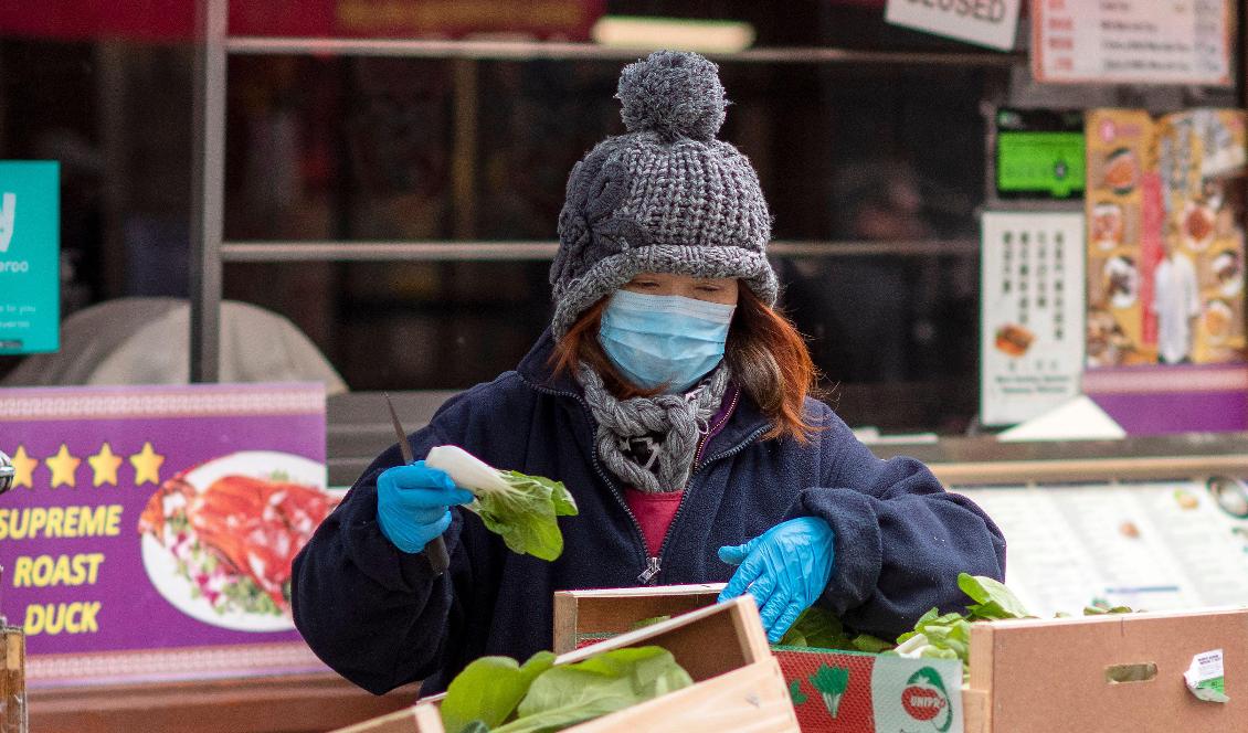 En kvinna bär ansiktsmask när hon arbetar på ett grönsaksstånd i China Town i London den 4 feb, 2020. Foto: Justin Tallis, AFP via Getty Images