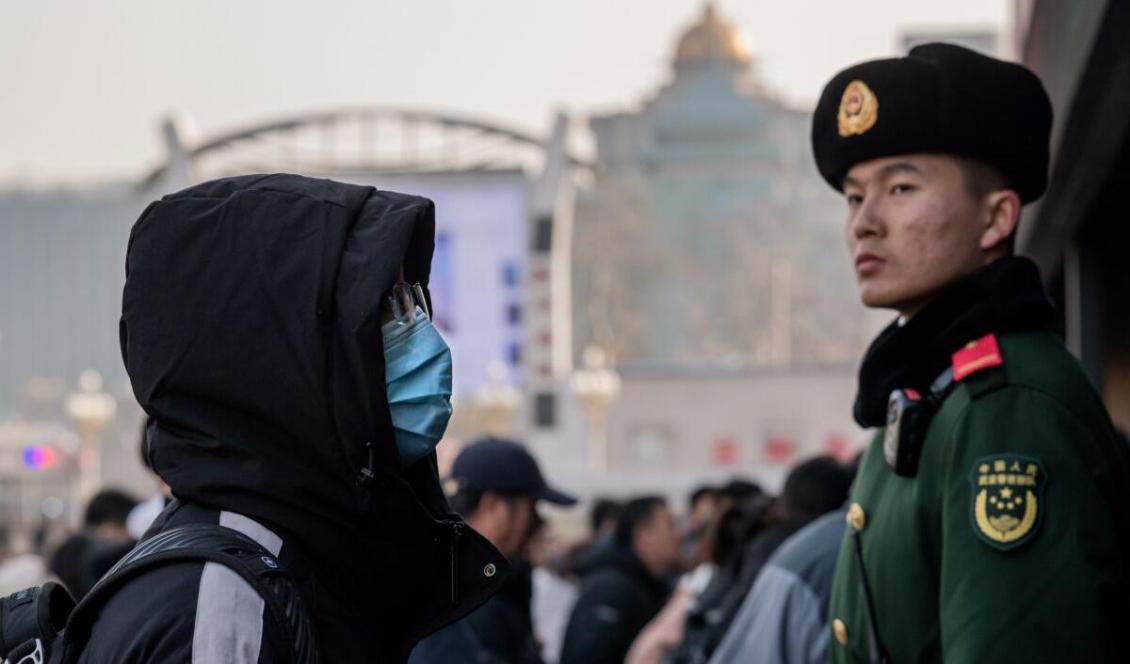 En man i munskydd intill en paramilitär polisman vid en tågstation i Peking, den 21 januari 2020. Foto: Nicolas Asfouri/AFP via Getty Images