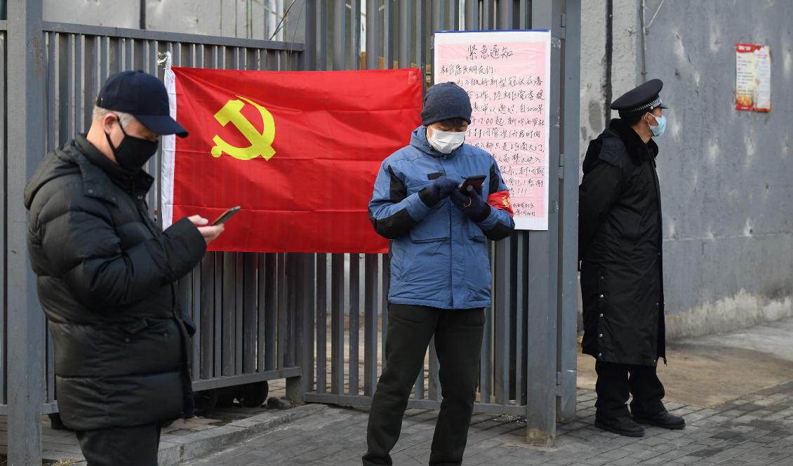 Tre personer med ansiktsmask står bredvid en kommunistisk flagga vid en byggnad i Peking i Kina den 9 februari 2020. Foto: Greg Baker/AFP via Getty Images