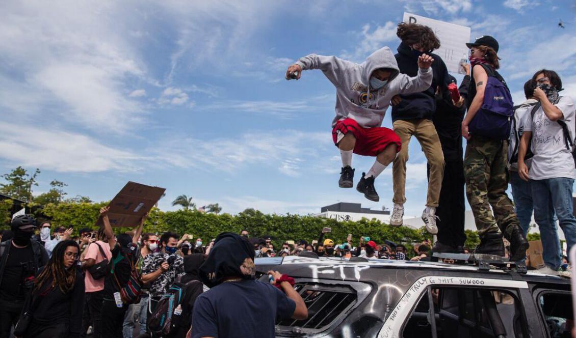 Demonstranter hoppar på en demolerad polisbil i Los Angeles den 30 maj 2020, under en protest i samband med den svarte mannen George Floyds död. Foto: Ariana Drehsler, AFP via Getty Images.