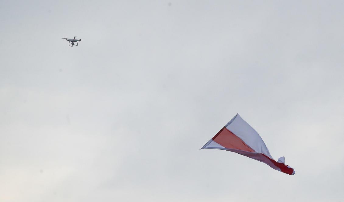 En drönare syns på himlen i Belarus huvudstad Minsk under en regimkritisk demonstration den 23 augusti. Landets gamla vit-röda flagga används som symbol av oppositionen. Foto: Dmitri Lovetsky/AP/TT