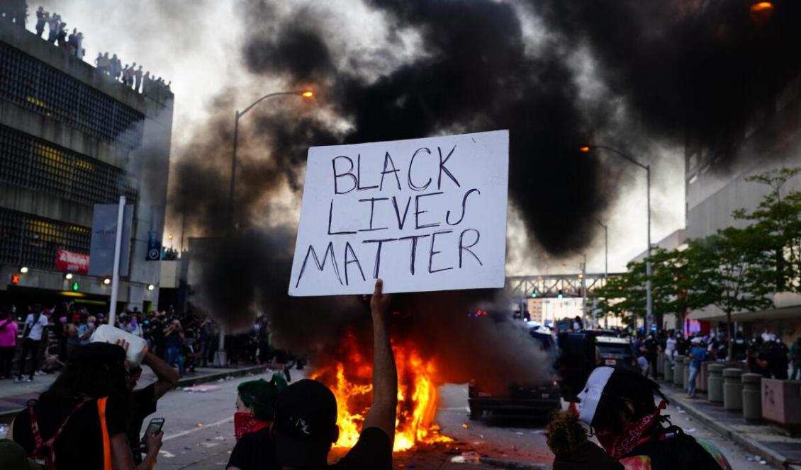En man håller en Black Lives Matter-skylt framför en brinnande polisbil under en protest utanför CNN Center, i Atlanta, Georgia, USA, den 29 maj 2020. Foto: Elijah Nouvelage/Getty Images