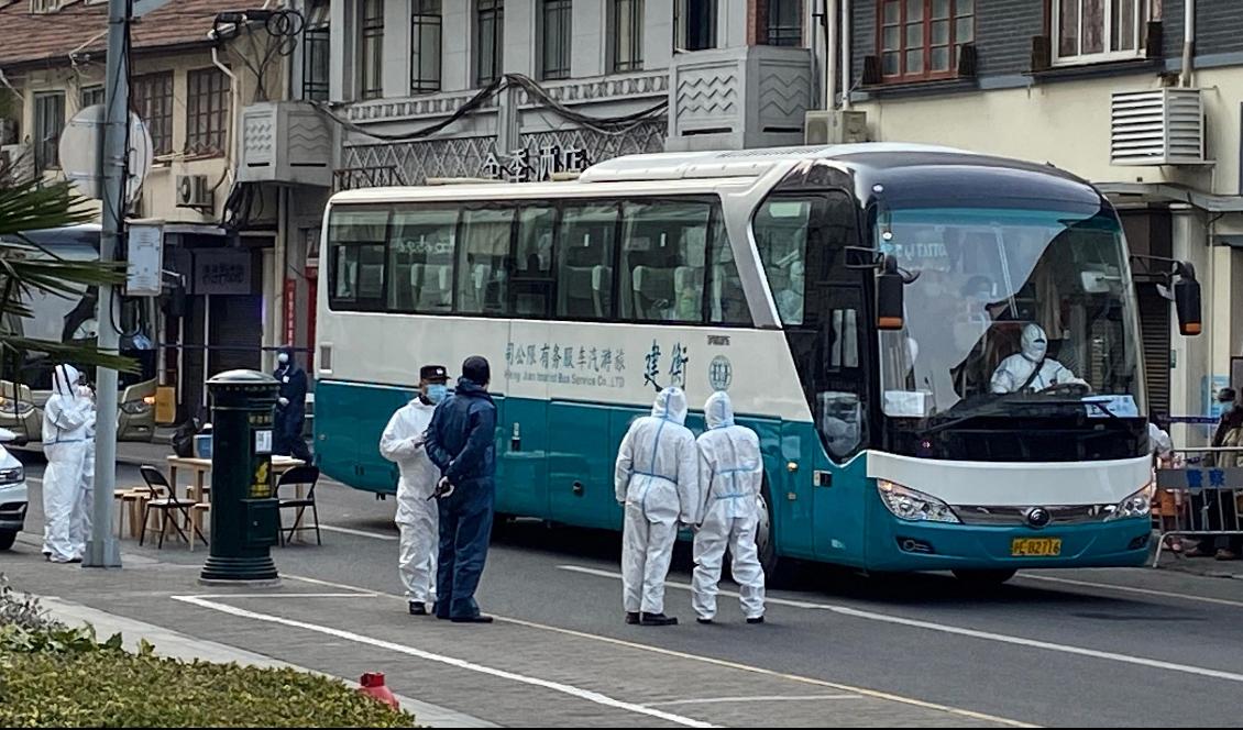 Polis och arbetare med skyddskläder vid en buss där invånare i Huangpudistriktet i Shanghai den 21 januari 2021 evakueras efter flera nya virusfall. Foto: STF/AFP via Getty Images