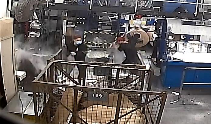 En skärmdump från en övervakningskamera. På bilden syns två män i svart, varav en håller en slägga, vandalisera tryckeriutrustning på Epoch Times Hongkongutgåva den 12 april 2021. Foto: Epoch Times