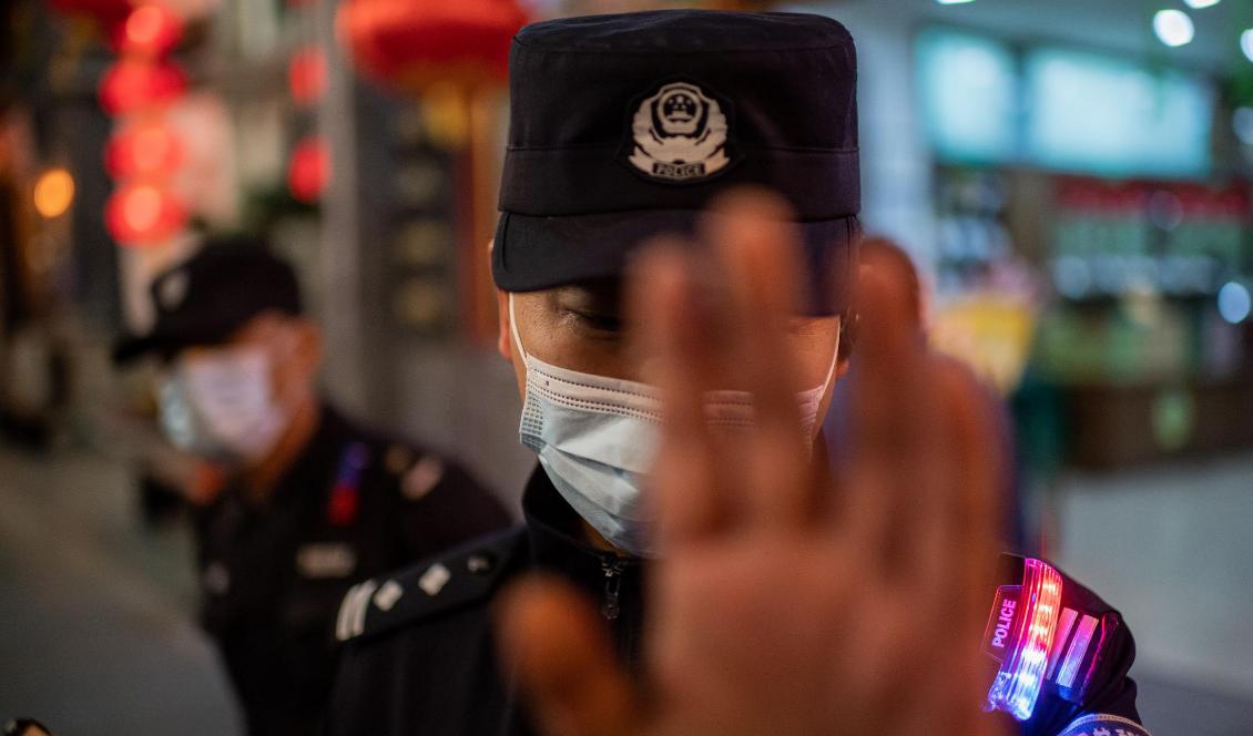 En polisman med munskydd försöker stoppa en journalist från att ta bilder utanför en galleria i Peking i Kina den 13 oktober 2020. Foto: Nicolas Asfouri/AFP via Getty Images