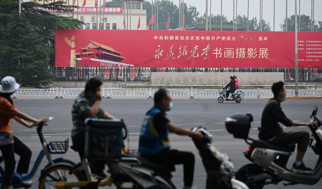 Folk åker förbi en banderoll som satts upp inför kommunistpartiets 100-årsdag. Texten lyder ”Följ partiet för alltid”. Peking den 9 juni 2021. Foto: 
Greg Baker/AFP via Getty Images