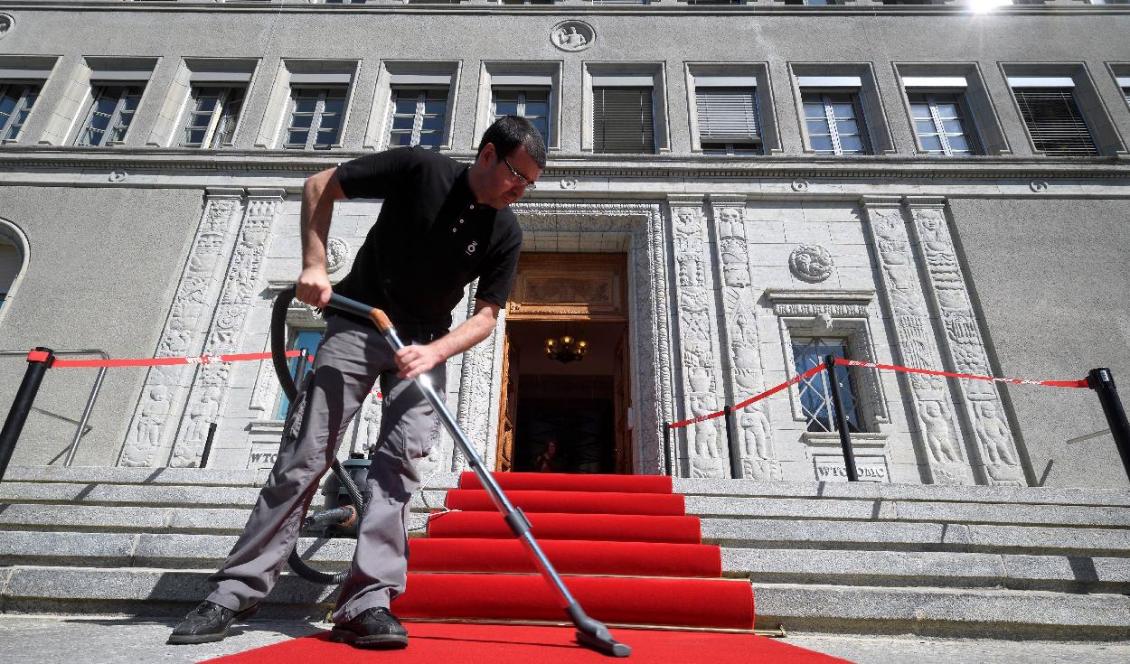 En man dammsuger den röda mattan i samband med en välkomstceremoni vid Världshandelsorganisationens (WTO) högkvarter i Genève. Foto: Fabrice Coffrini/AFP via Getty Images