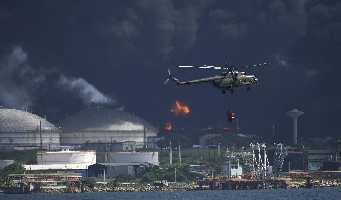 En helikopter har satts in för att vattenbomba branden i ett oljelager i Matanzas på Kuba. Foto: Ramon Espinosa/AP/TT