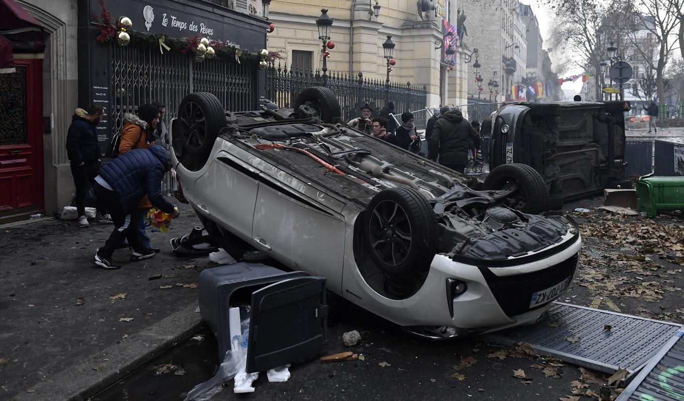 Människor går förbi bilar som välts omkull efter en kurdisk demonstration som mynnade ut i upplopp och oroligheter i Paris på julafton den 24 december 2022. Foto: Julien De Rosa/AFP via Getty Images