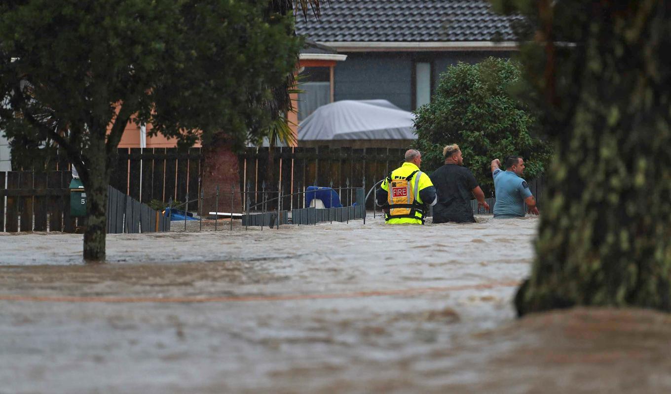 Personal från räddningstjänsten och en civilperson vadar genom vattenmassorna i Auckland på fredagen. Foto: Hayden Woodward/AP/TT