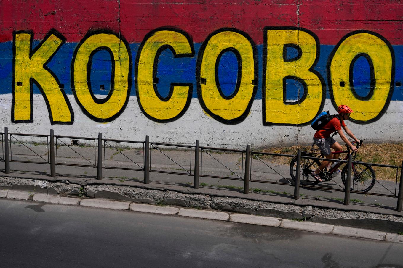 En man cyklar förbi en väggmålning i Serbiens huvudstad Belgrad med texten "Kosovo" målat ovanpå den serbiska flaggans färger. Arkivbild. Foto: Darko Vojinovic/AP/TT