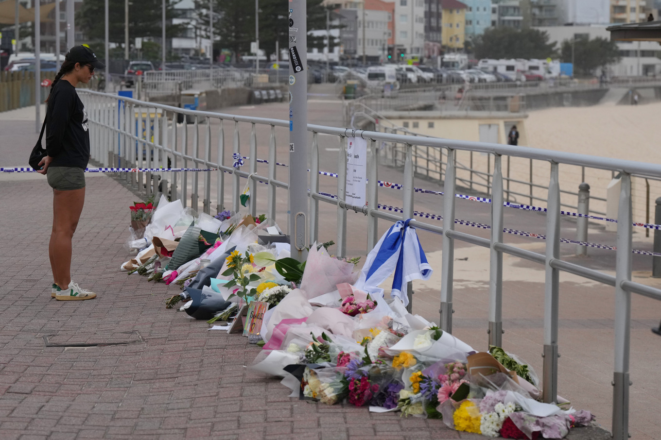 En förbipasserande på Bondi Beach tittar på blommor som placerats ut. Foto: Mark Baker/AP/TT